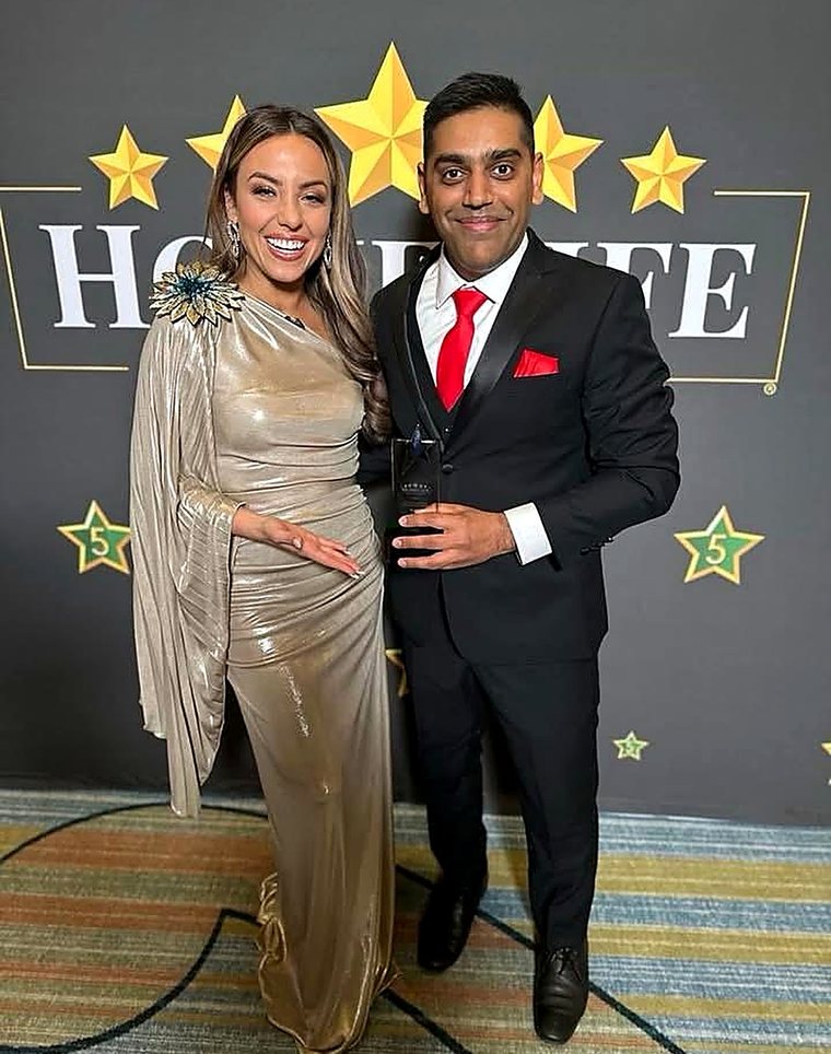 Robin Patel with a guest at the HomeLife awards, holding a glass award in front of the backdrop.