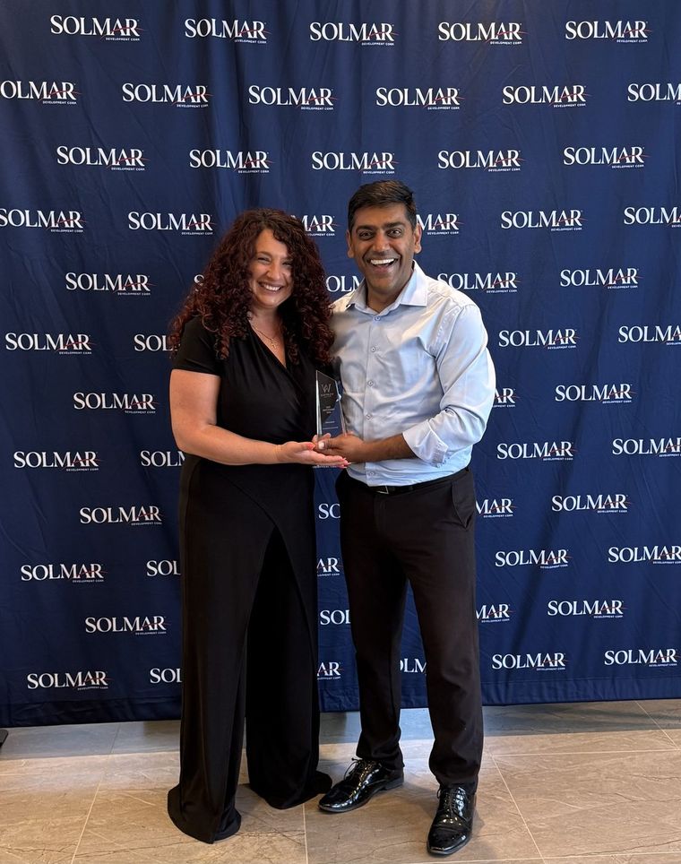 Robin Patel receiving a glass award in front of a Solmar backdrop.